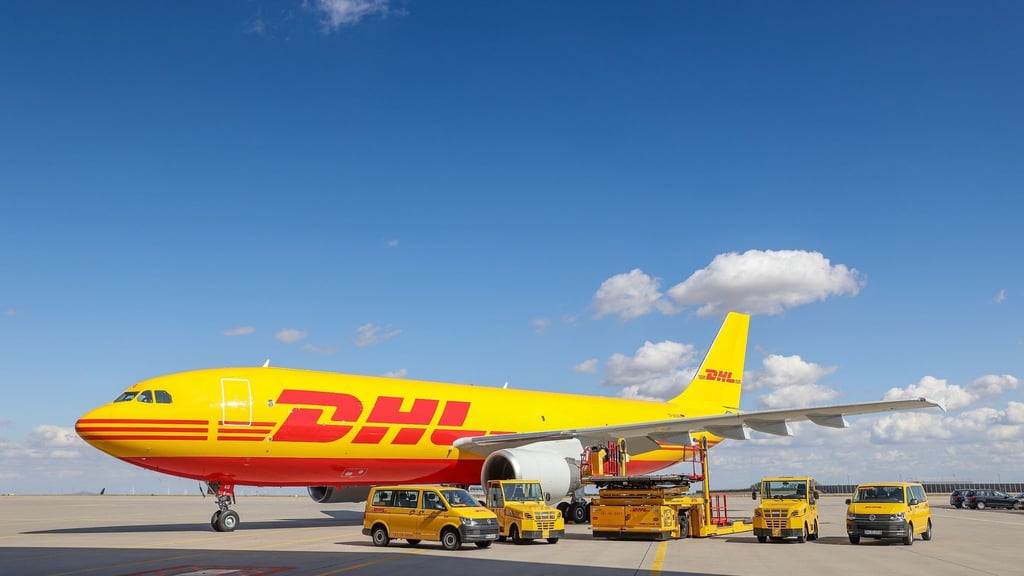 Ein Frachtflugzeug von DHL und verschiedene Fahrzeuge für die Logistik stehen auf dem Vorfeld auf dem Flughafen Leipzig/Halle.