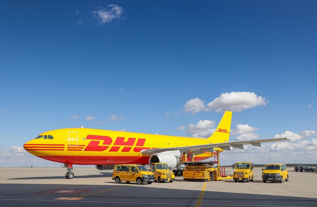 Ein Frachtflugzeug von DHL und verschiedene Fahrzeuge für die Logistik stehen auf dem Vorfeld auf dem Flughafen Leipzig/Halle.