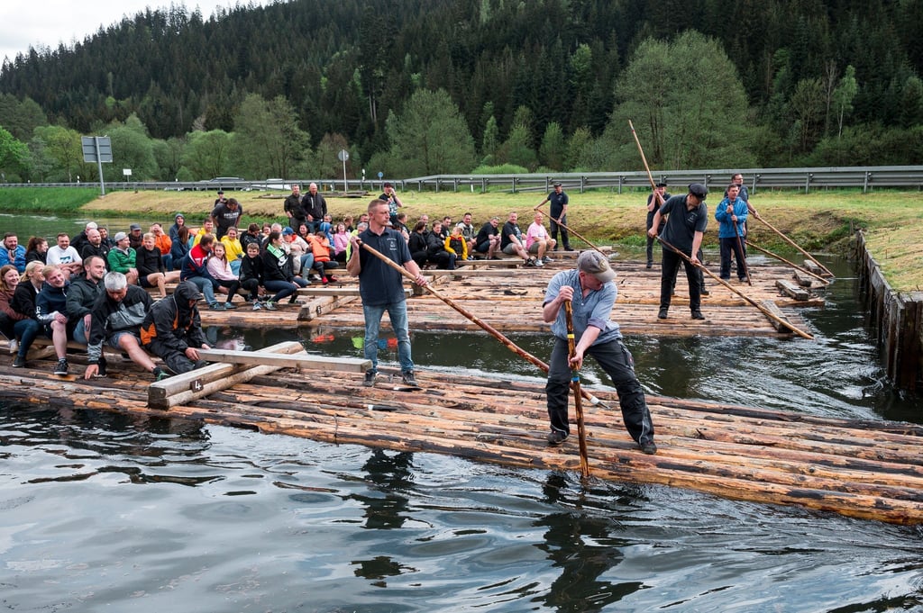 Zwei Flößer steuern das Floß mit einem Floßhaken durch die Schleuse und den Fluss entlang.