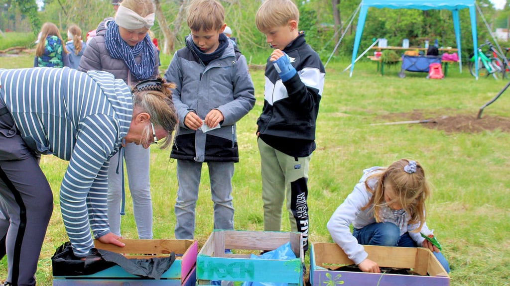 Heike Jaworski erklärt den Ferienkindern beim Gärtnern im Gemeindegarten, wie verschiedener Gemüsesamen richtig ins Erdreich der selbst hergestellten Mini-Hochbeete gebracht werden soll.