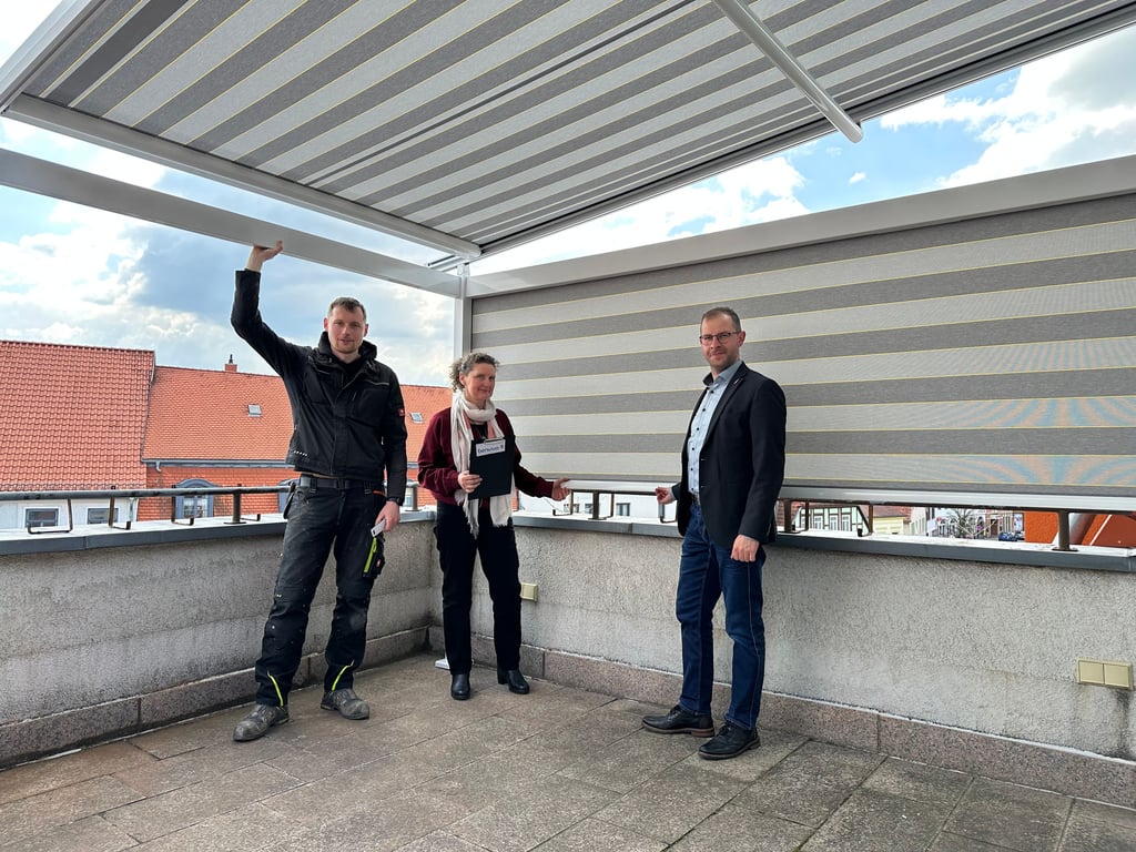 Auf der Benvivo-Dachterrasse lässt es sich jetzt dank einer Markise auch im Sommer aushalten, wie Robert Wille von der gleichnamigen Firma, Silke Kirchhof und Bürgermeister Philipp Stark feststellen.