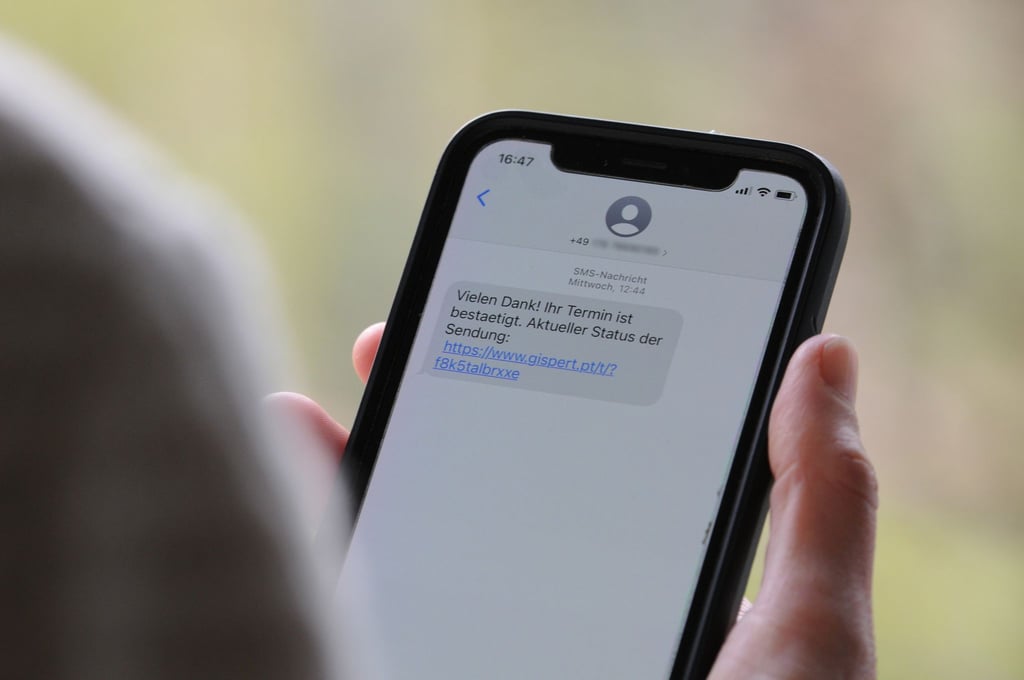 Eine Frau hält ein Smartphone in der Hand, auf dessen Display eine Betrugs-SMS zu lesen ist.