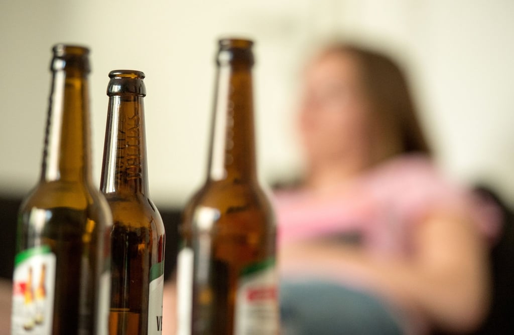Eine junge Frau sitzt hinter leeren Bierflaschen.