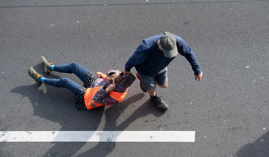 Ein Verkehrsteilnehmer (r) zieht bei einer Blockade der Letzten Generation auf der Autobahn 100 eine Aktivistin von der Straße.