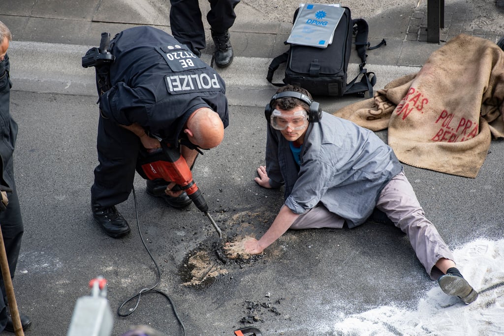 Polizist meißelt Klima-Kleber vom Asphalt.