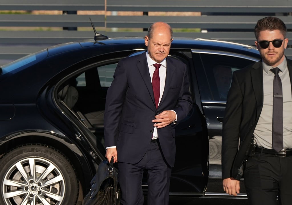 Bundeskanzler Olaf Scholz (l, SPD) kommt zum Start einer zweitägigen Reise auf dem militärischen Teil des Flughafens Berlin Brandenburg BER an und steigt aus einer Limousine.