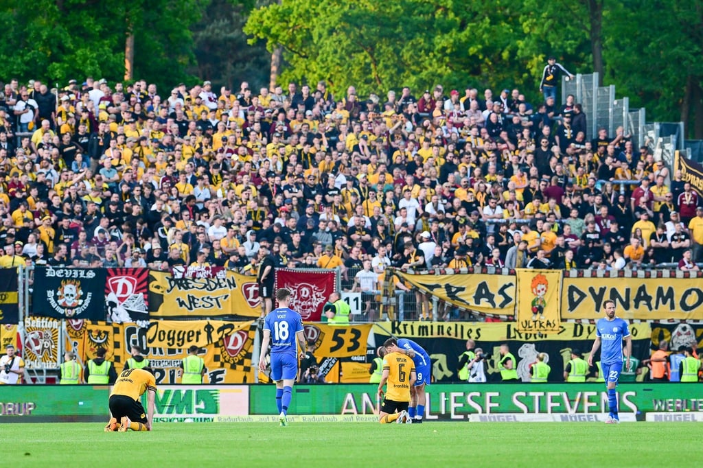Enttäuschte Dresdner Spieler knien auf dem Rasen vor dem eigenen Fanblock.