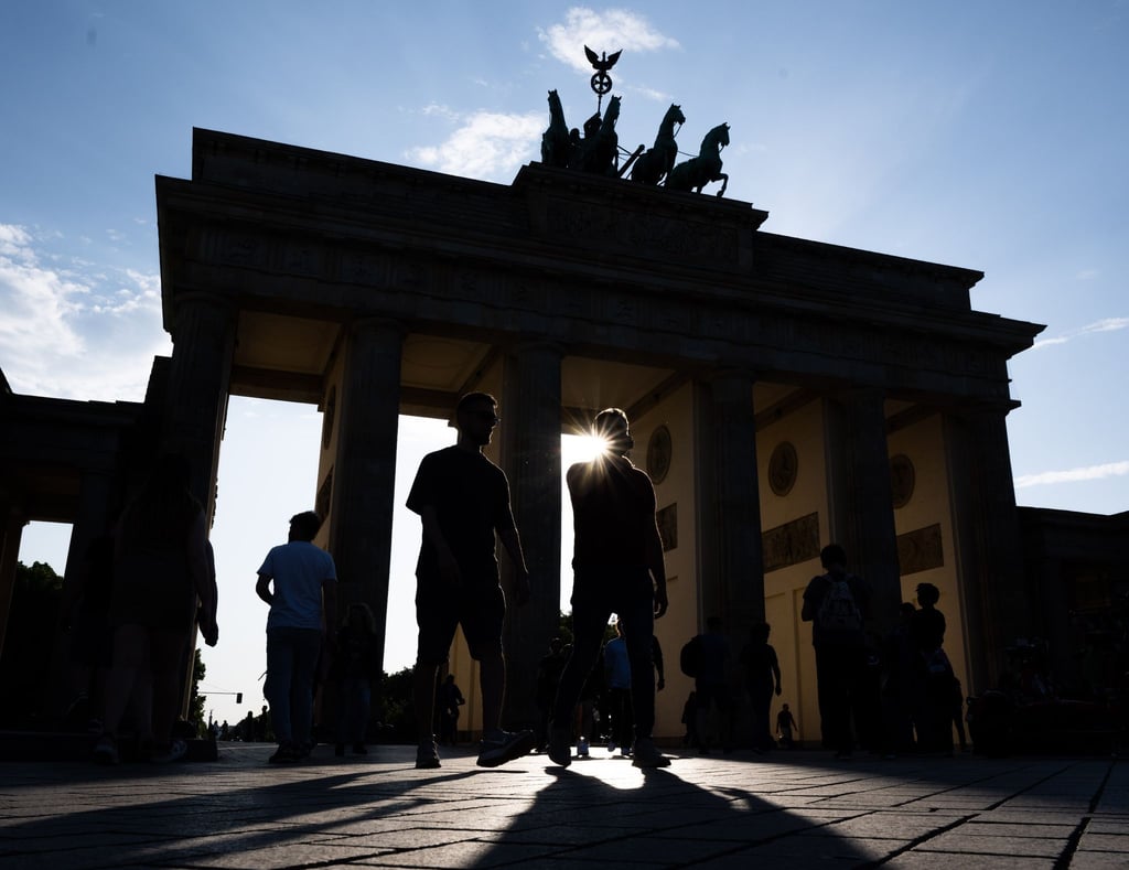 Touristen gehen im Gegenlicht der untergehenden Sonne über den Pariser Platz vor der Kulisse vom Brandenburger Tor.