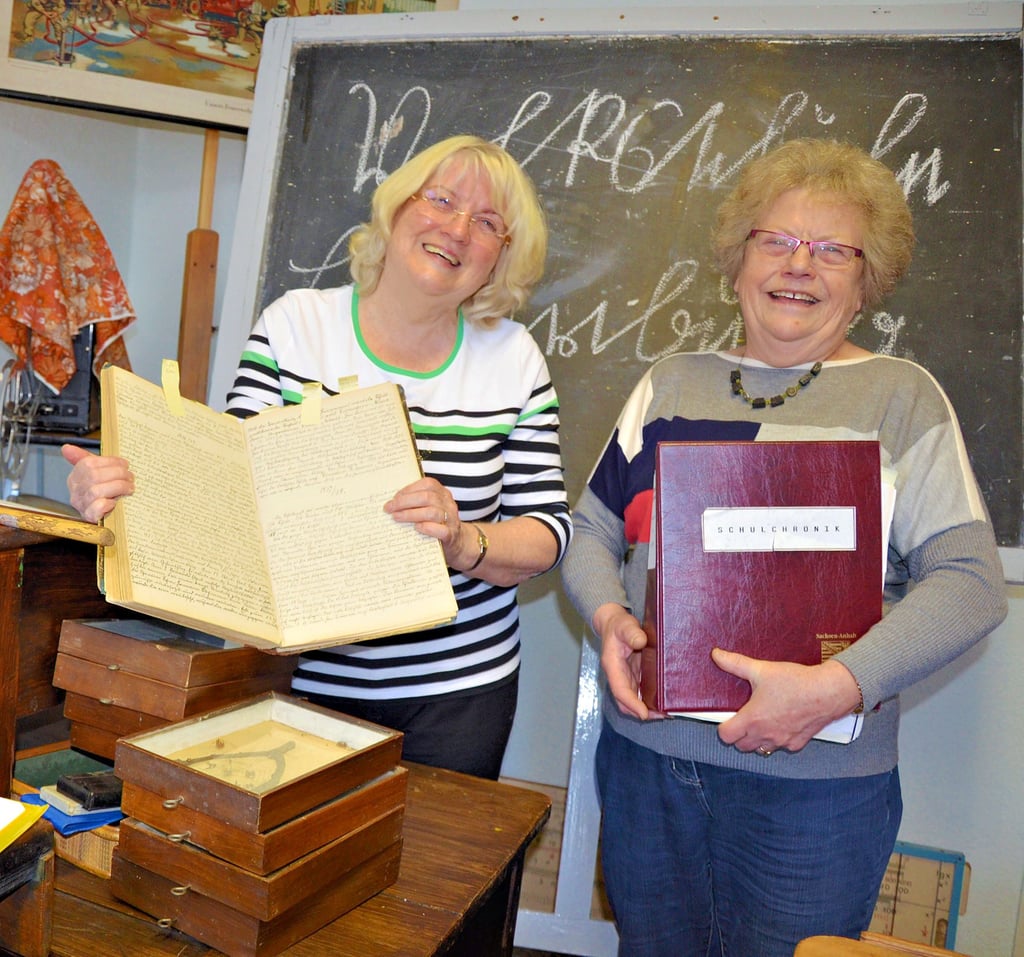 Helga Dornemann (rechts) in gewohnter Pose. Mit einem Strahlen im Gesicht zeigt sie den liebevoll hergerichteten Klassenraum in der Heimatstube in Löderburg, der veranschaulicht, wie Klassenräume bis nach dem Zweiten Weltkrieg ausgesehen haben.