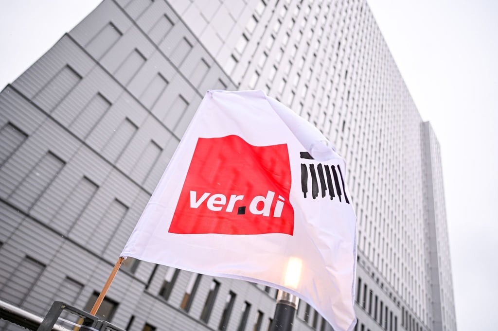 Eine Flagge von Verdi weht bei einem Warnstreik vor einem Hochhaus.