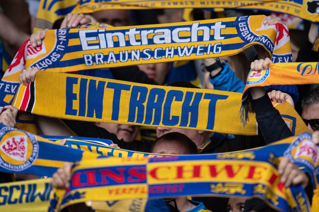 Fans von Eintracht Braunschweig stehen mit ihren Schals auf der Tribüne.