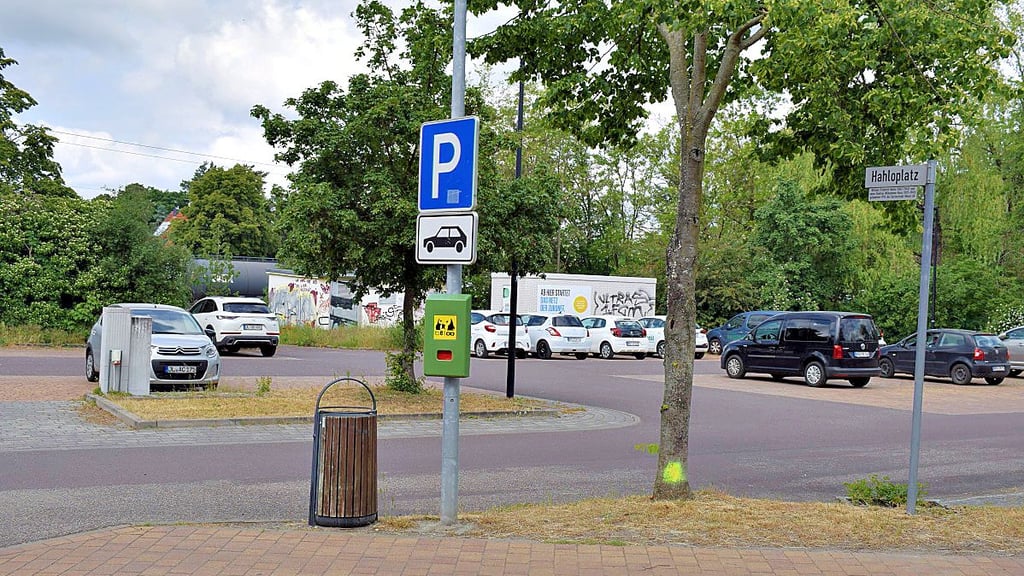 Der Hahloplatz unweit des Bahnhofs bietet Stellplätze für Pkw an. Am Eiscafé weist ein neues Schild auf den Parkplatz hin.