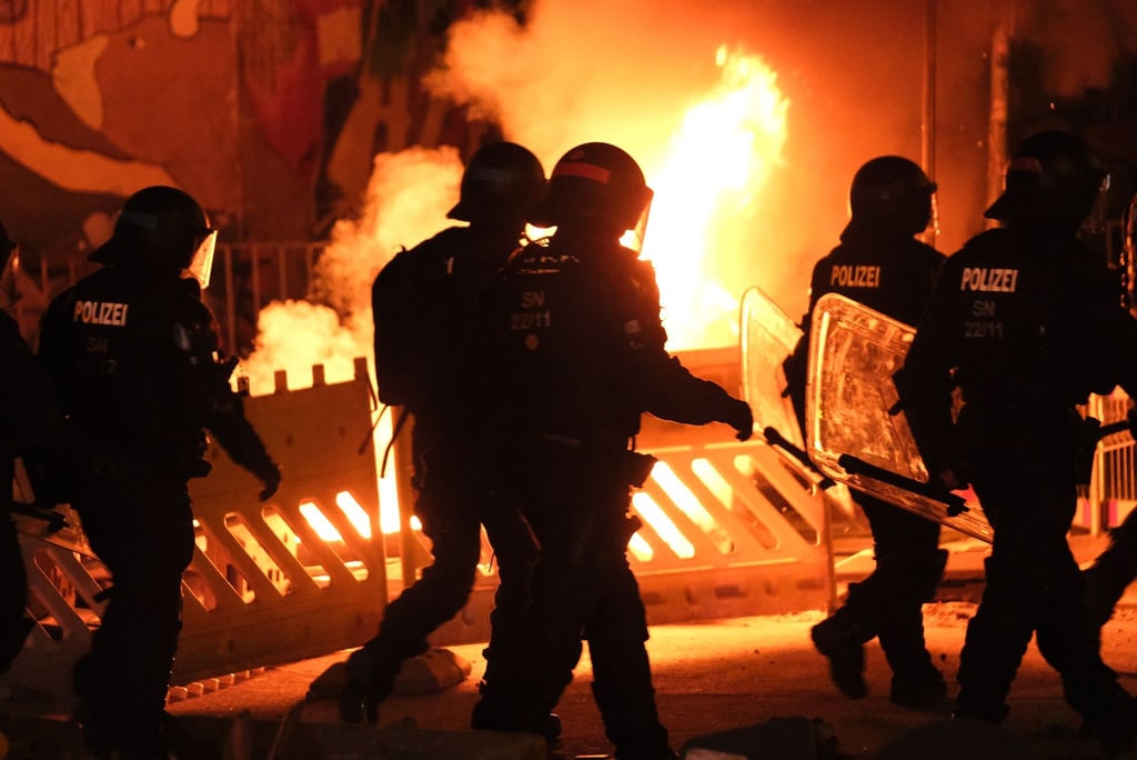 Polizisten gehen an einer brennenden Barrikade vorbei.