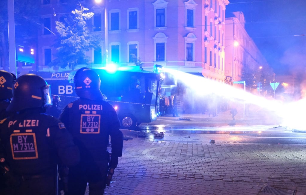 Ein Wasserwerfer löscht brennende Gegenstände auf einer Fahrbahn.