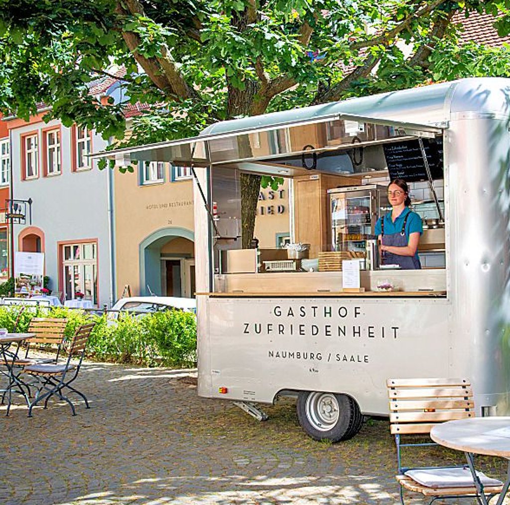Ein Food-Truck des „Gasthofs Zufriedenheit“ steht samt Tischen und Stühlen auf der kleinen Insel am Steinweg.