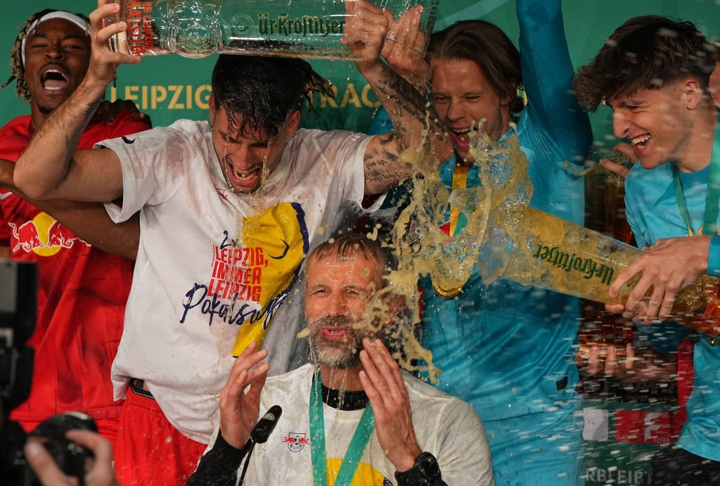 Leipzigs Spieler übergießen Trainer Marco Rose mit Bier während der Pressekonferenz.