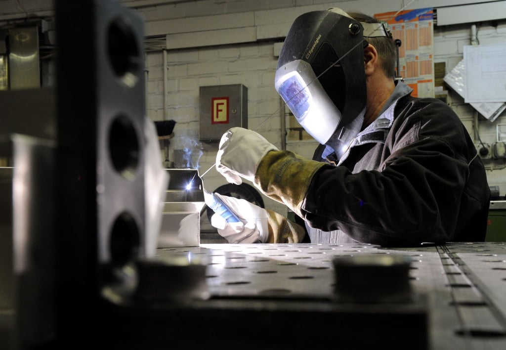 Ein Mitarbeiter eines metallverarbeitenden Betriebes schweißt eine Naht an einem Werkstück.