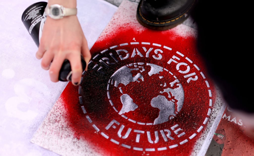 Eine Klimaaktivistin sprüht während einer Kundgebung ein Logo der Bewegung Fridays For Future auf ein Transparent.