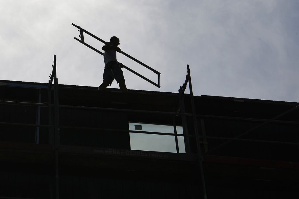 Ein Arbeiter trägt auf einer Baustelle ein Teil eines Baugerüsts.