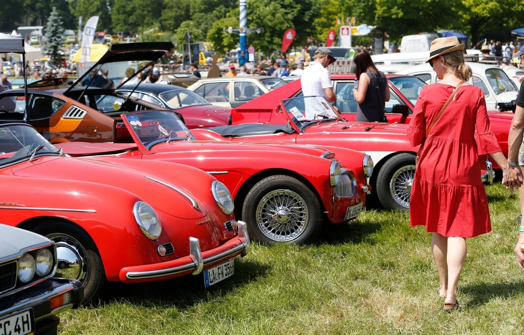 Eine Frau im roten Kleid betrachtet historische Sportwagen bei Südbayerns größtem Oldtimer-Treffen vor dem fast 500 Jahre alten Schloss Maxlrain.