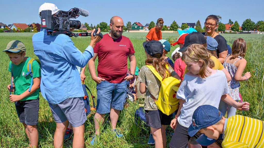 Biobauer Jonas Schulze-Niehoff aus Schleibnitz erklärt bei dem Filmaufnahmen von einem TV-Team des MDR einer dritten Klasse der Freien Waldorfschule die Feldfrüchte auf seinem Acker.