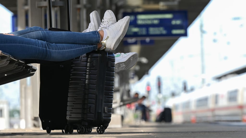 Zwei Reisegäste warten an einem Bahnhof am Gleis.