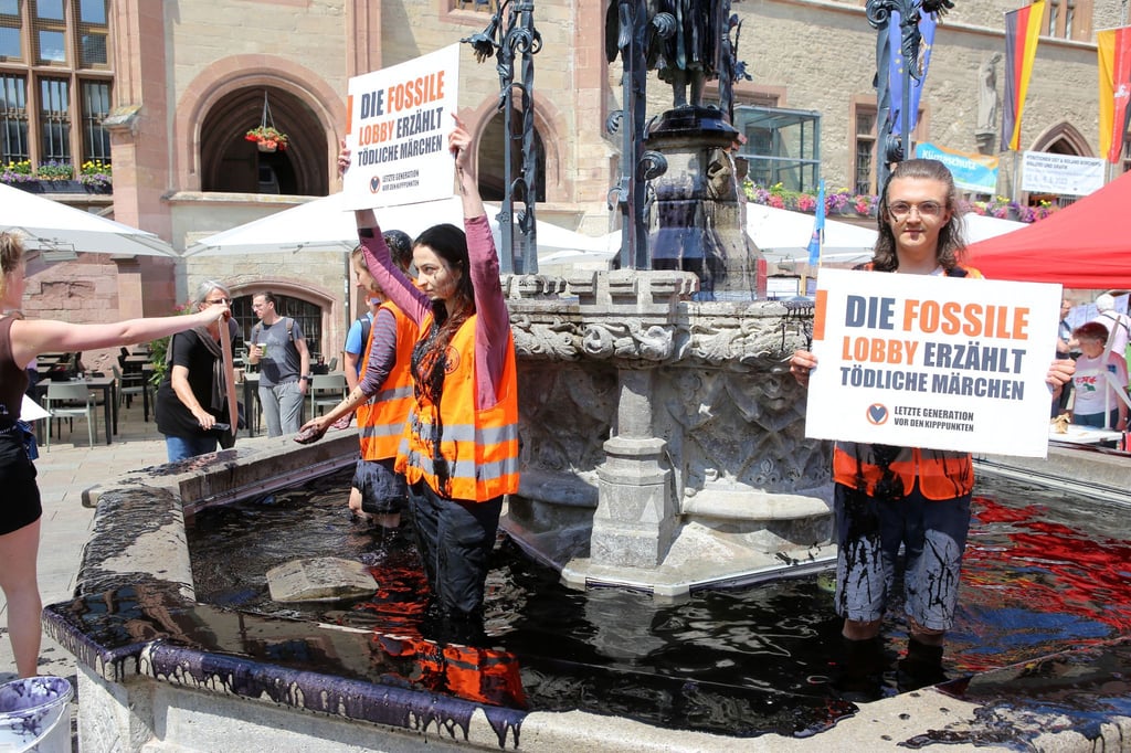 Klima-Aktivisten der Gruppe „Letzte Generation“ stehen zum Auftakt der Klimaschutztage im Gänseliesel-Brunnen.