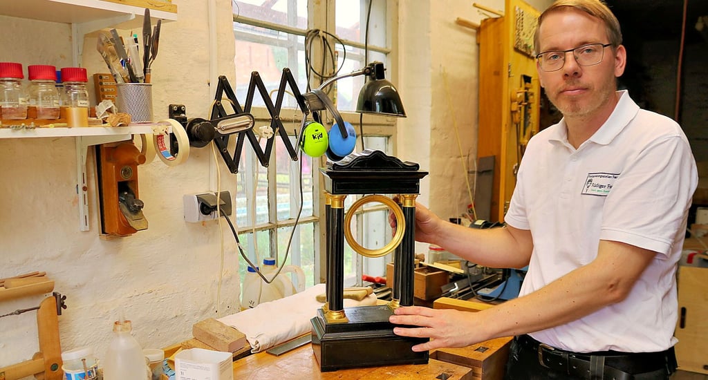 Restaurator Rüdiger Faust in seiner Werkstatt mit einer Uhr im Empire-Stil.