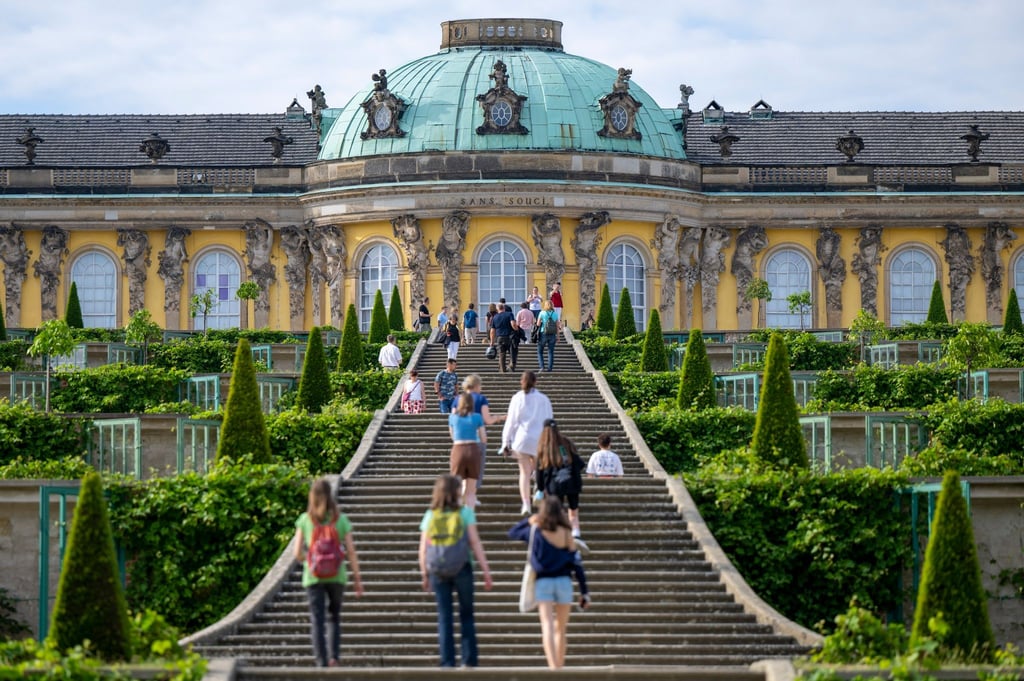Zahlreiche Besucher stehen im Park Sanssouci auf der Treppe vor dem Schloss Sanssouci.