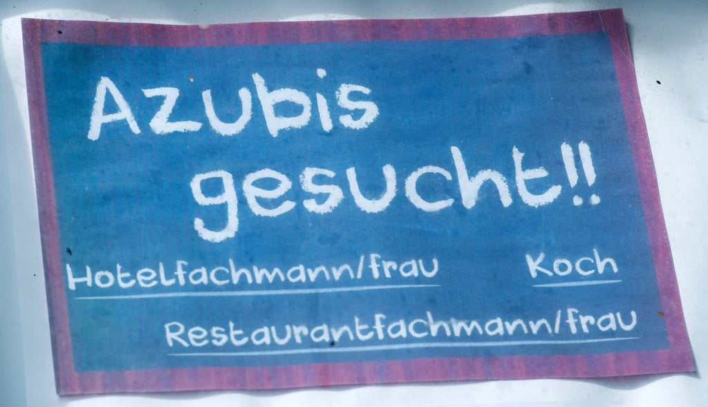 Vor einem Hotel hängt ein Schild mit dem Schriftzug „Azubis gesucht!!“.