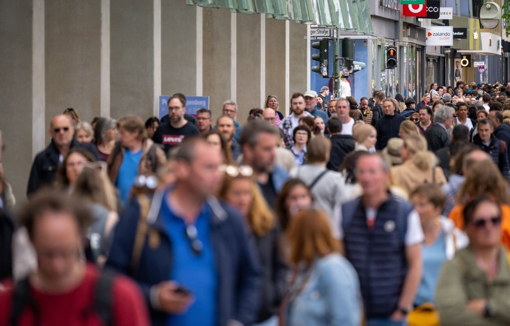 Zahlreiche Menschen gehen an Geschäften in einer Einkaufsstraße vorbei.