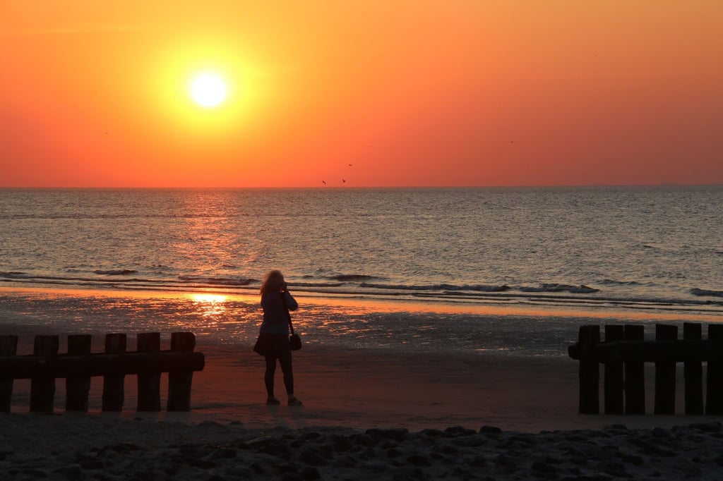 Eine Frau fotografiert am Strand der Insel Wangerooge einen Sonnenuntergang über der Nordsee.