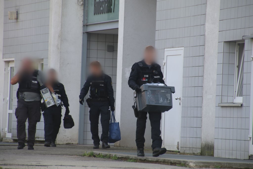 Ermittler tragen Taschen einen PC und eine Kiste aus dem Haus in der Bodestraße in Halle-Neustadt.