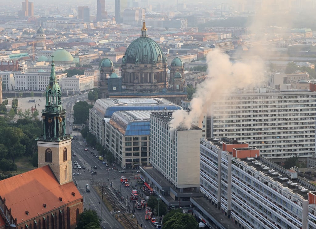 Rauch steigt aus einem Hochhaus, im Hintergrund der Berliner Dom.