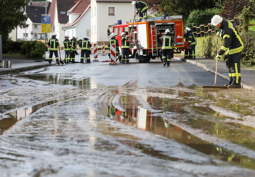 Einsatzkräfte der Feuerwehr reinigen eine überflutete und verschmutzte Straße.