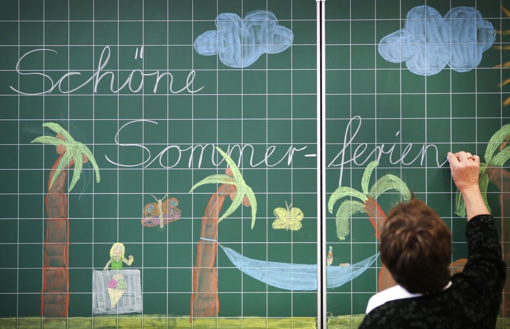 Eine Lehrerin schreibt „Schöne Sommer-ferien“ an eine Tafel in einer Grundschule.