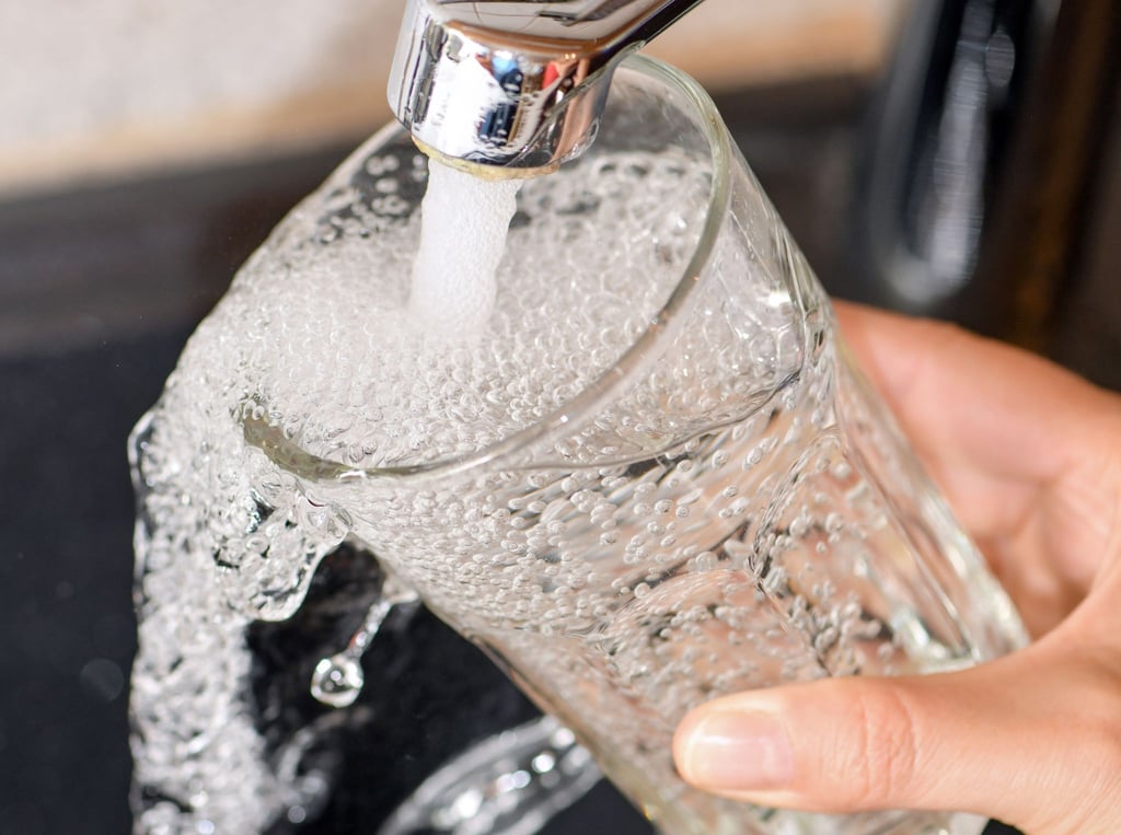 Am Wasserhahn in einer Küche wird ein Trinkglas mit Leitungswasser befüllt.