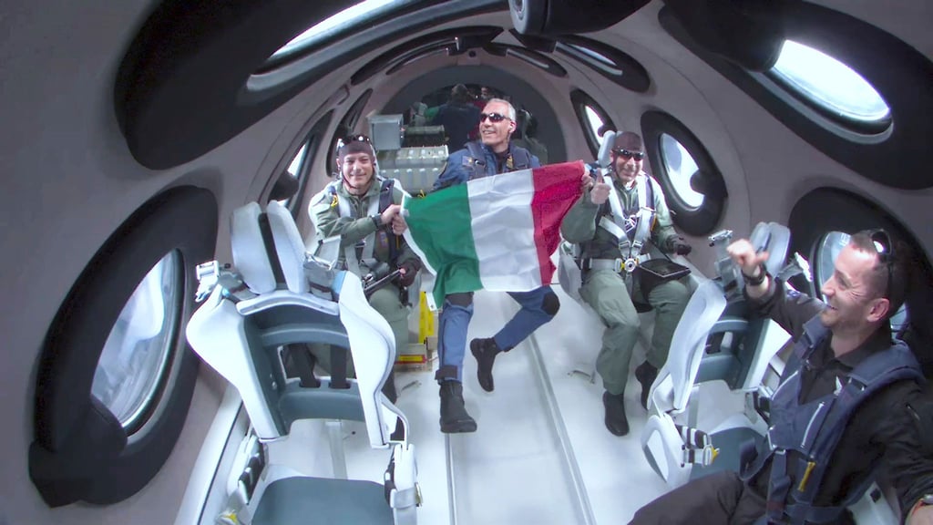 Walter Villadei (M), Wissenschaftler der italienischen Luftwaffe, hält eine italienische Fahne, während er und andere italienische Forscher einige Momente der Schwerelosigkeit an Bord des Raumflugzeugs von Virgin Galactic erleben.
