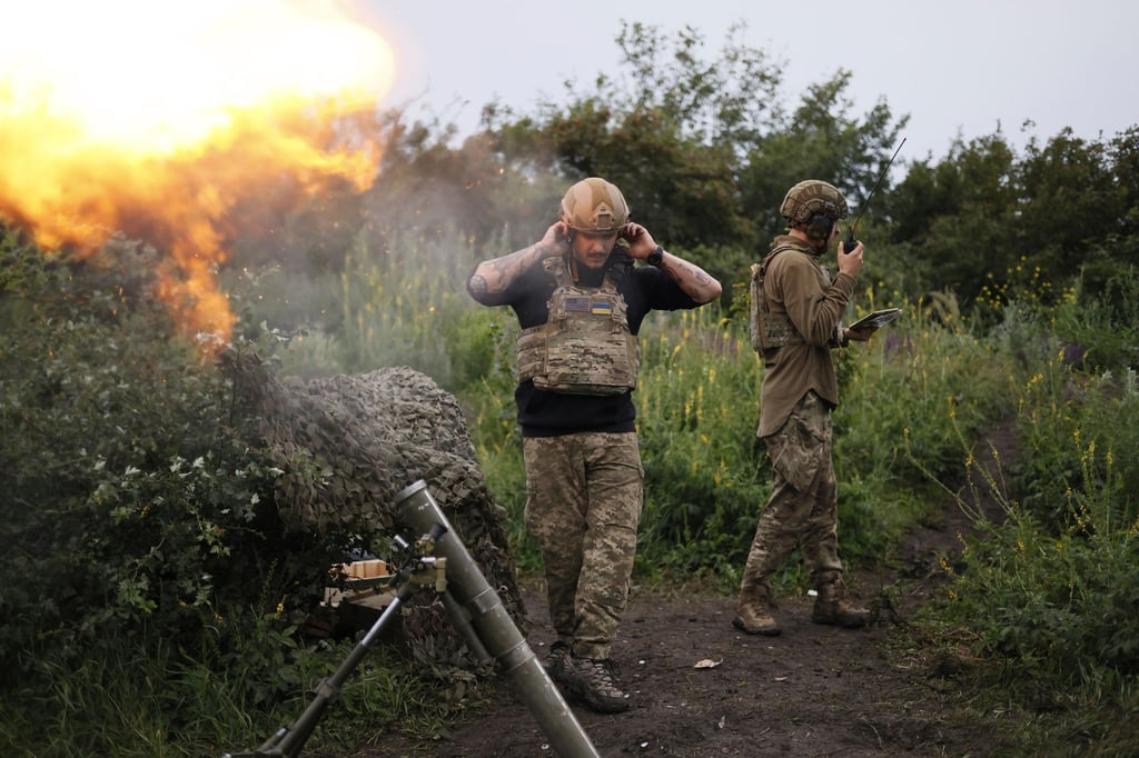Ein ukrainischer Soldat während eines Funkgesprächs, während ein anderer Soldat 82-mm-Mörser auf russische Stellungen feuert.
