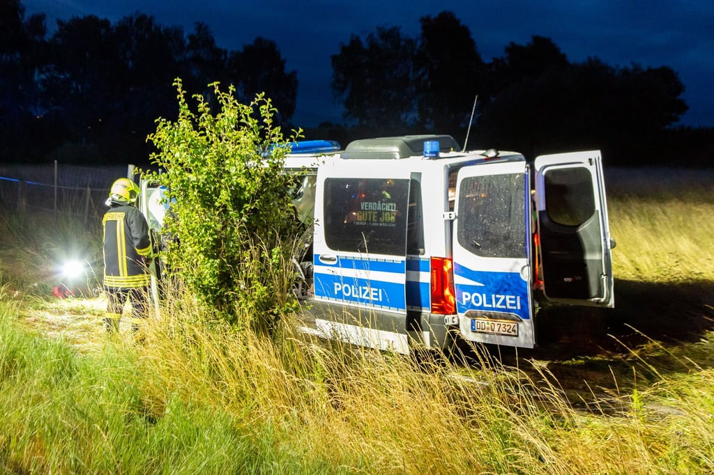 Ein Mannschaftswagen der Polizei steht in einem Grasfeld.