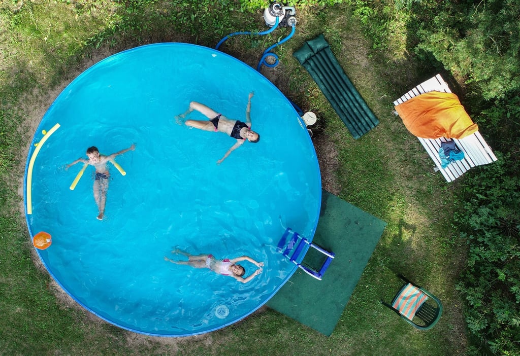 Drei Kinder planschen in einem Gartenpool (Luftaufnahme mit einer Drohne).