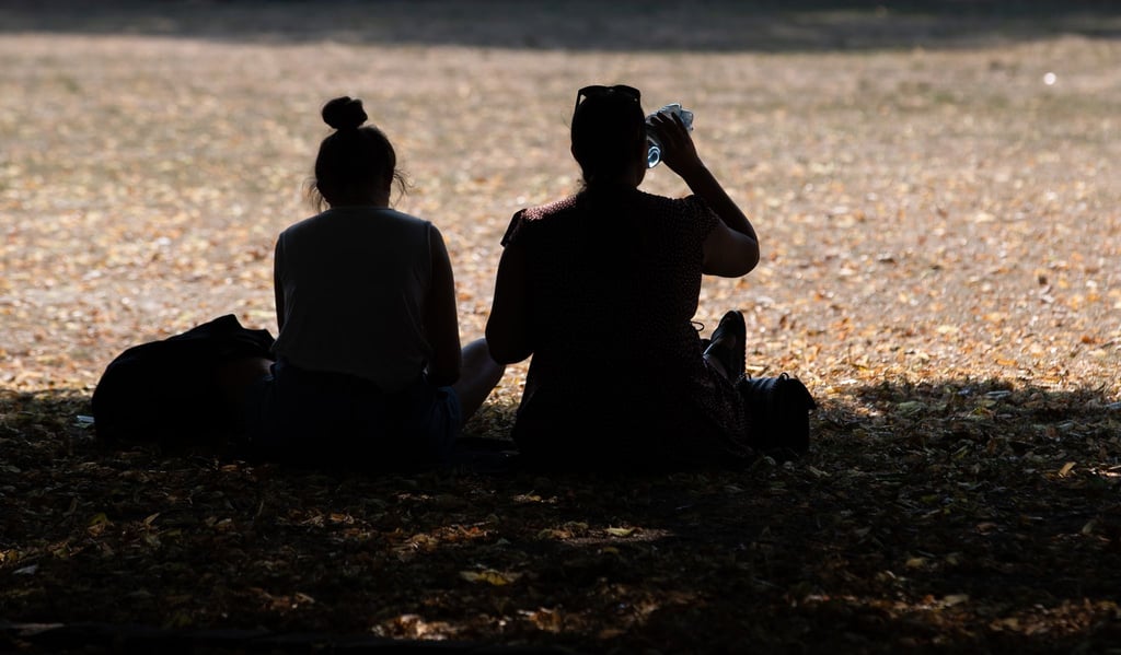 Zwei Frauen sitzen in einem Park im Schatten der Bäume, um sich vor der Hitze zu schützen.