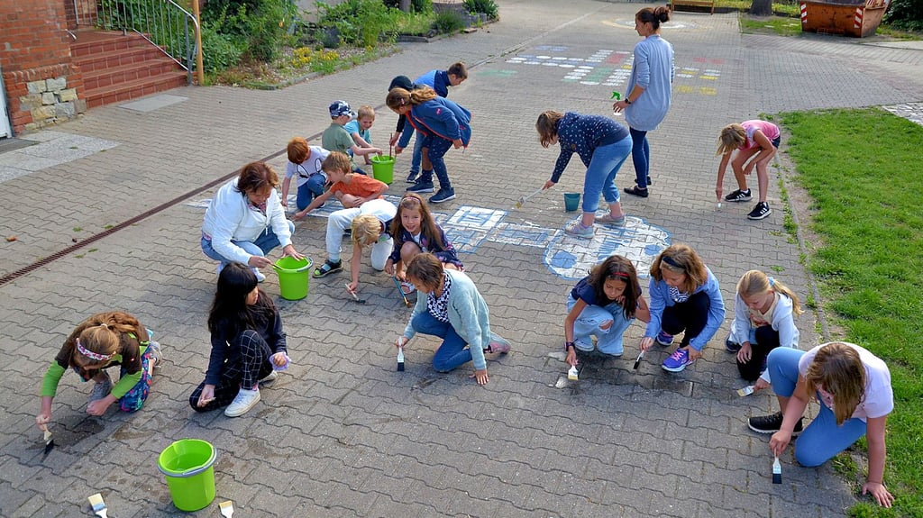 Mit viel Liebe zum Detail malen Mädchen und Jungen aus der ersten und zweiten Klasse der Grundschule Langenweddingen Bilder mit Wasser auf ihren Schulhof.