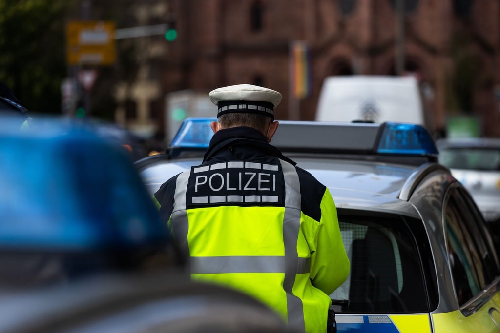 Ein Polizeibeamter steht zwischen zwei Einsatzfahrzeugen der Polizei.