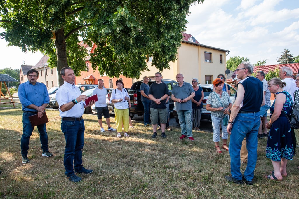 Auf der Grünfläche vor dem sanierten Dorfgemeinschaftshaus (Hintergund, Mitte) hört OB Armin Müller aufmerksam zu, was Janisrodas Ortsbürgermeister Guido Kühnert den Einwohnern und Gästen erzählt.