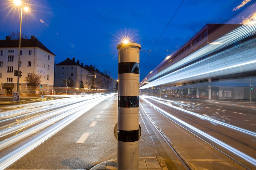 Eine Blitzsäule mit kombinierter Überwachung von Rotlicht und Geschwindigkeit steht an einer Ampelkreuzung (Langzeitbelichtung).