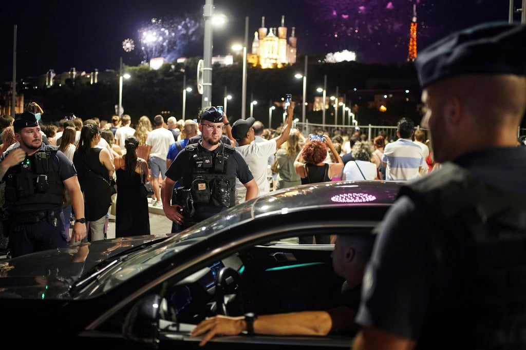 Polizisten kontrollieren einen Autofahrer in Lyon, während die Menschen ein Feuerwerk zum Tag der Bastille beobachten.