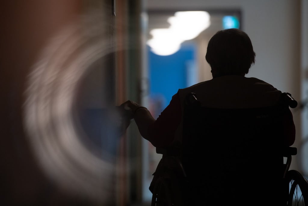 Eine Frau sitzt in einem Alten- und Pflegeheim in einem Rollstuhl auf einem Gang.