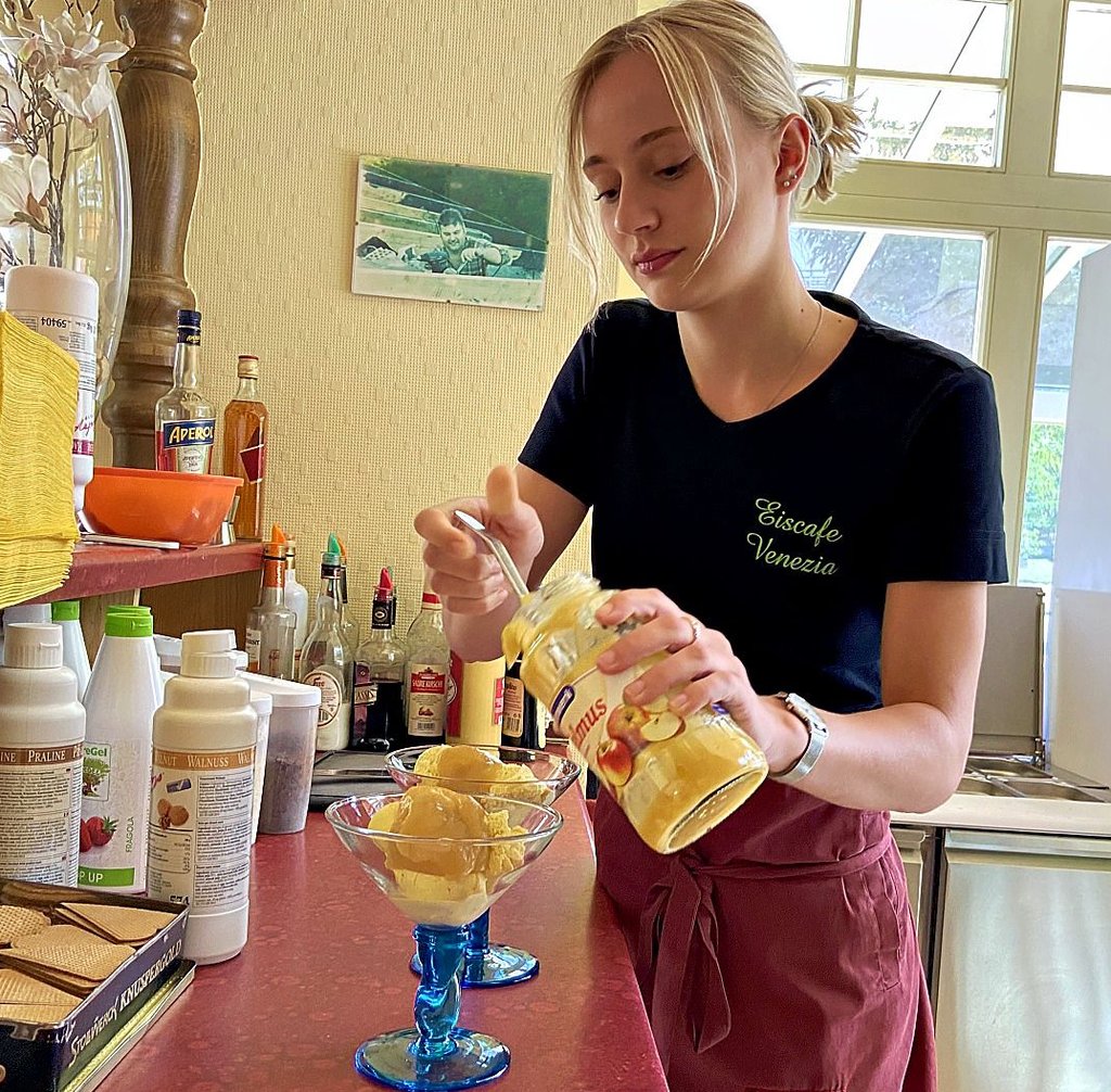 Amelie Jortzik bereitet zwei Eisbecher zu. Zudem betreut sie die Laufkundschaft am nach außen gerichteten Eistresen.