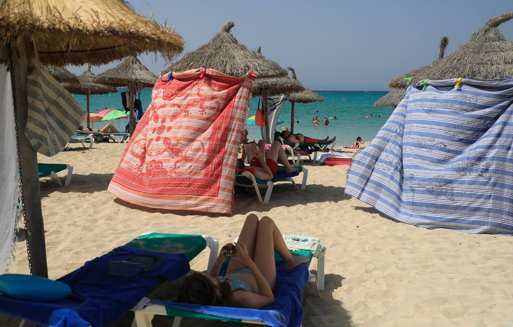 Menschen schützen sich bei extremer Hitze mit Strandtüchern vor der Sonne am Strand von Arenal.